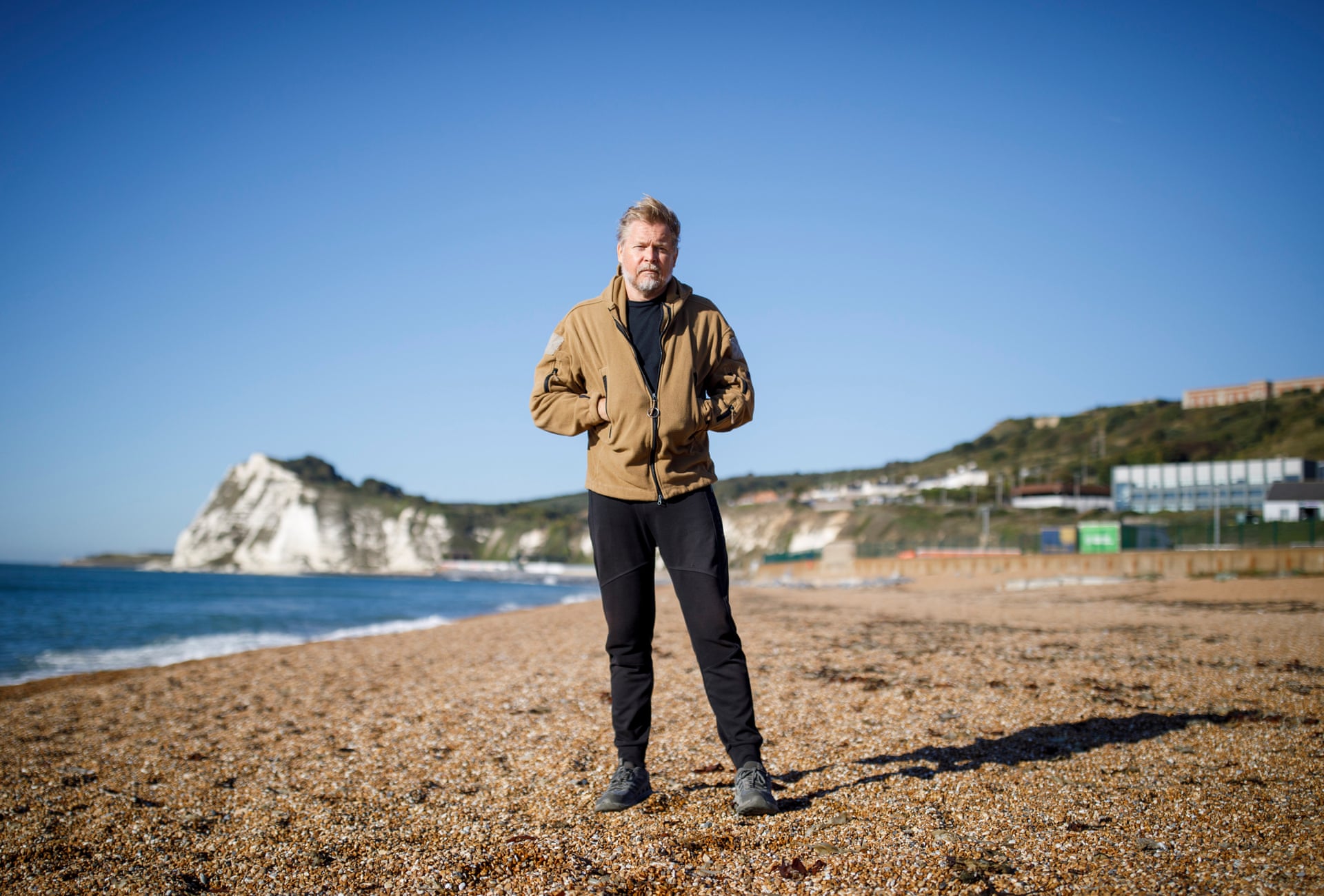 Karl Bushby stands on the pebble beach at Dover, with the sea and white cliffs behind him.